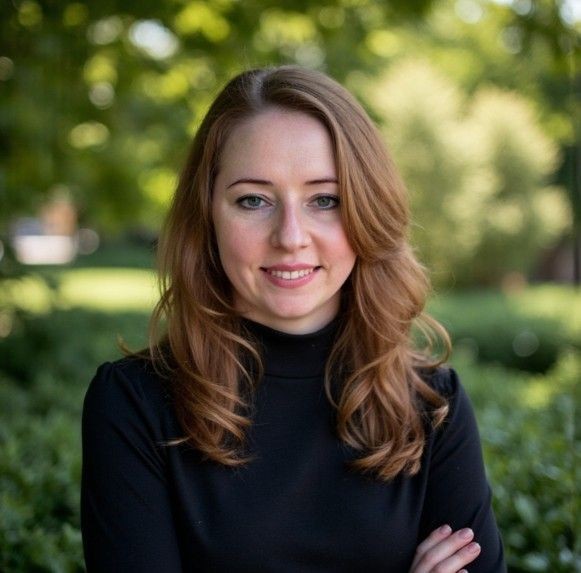 Woman with long hair wearing a black top, standing in a garden with greenery in the background.